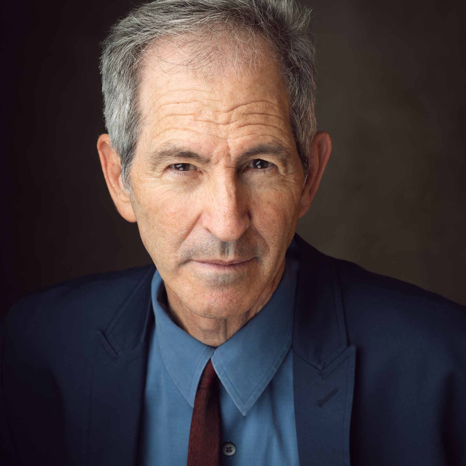 Actor portrait of an older man in a navy suit and blue shirt