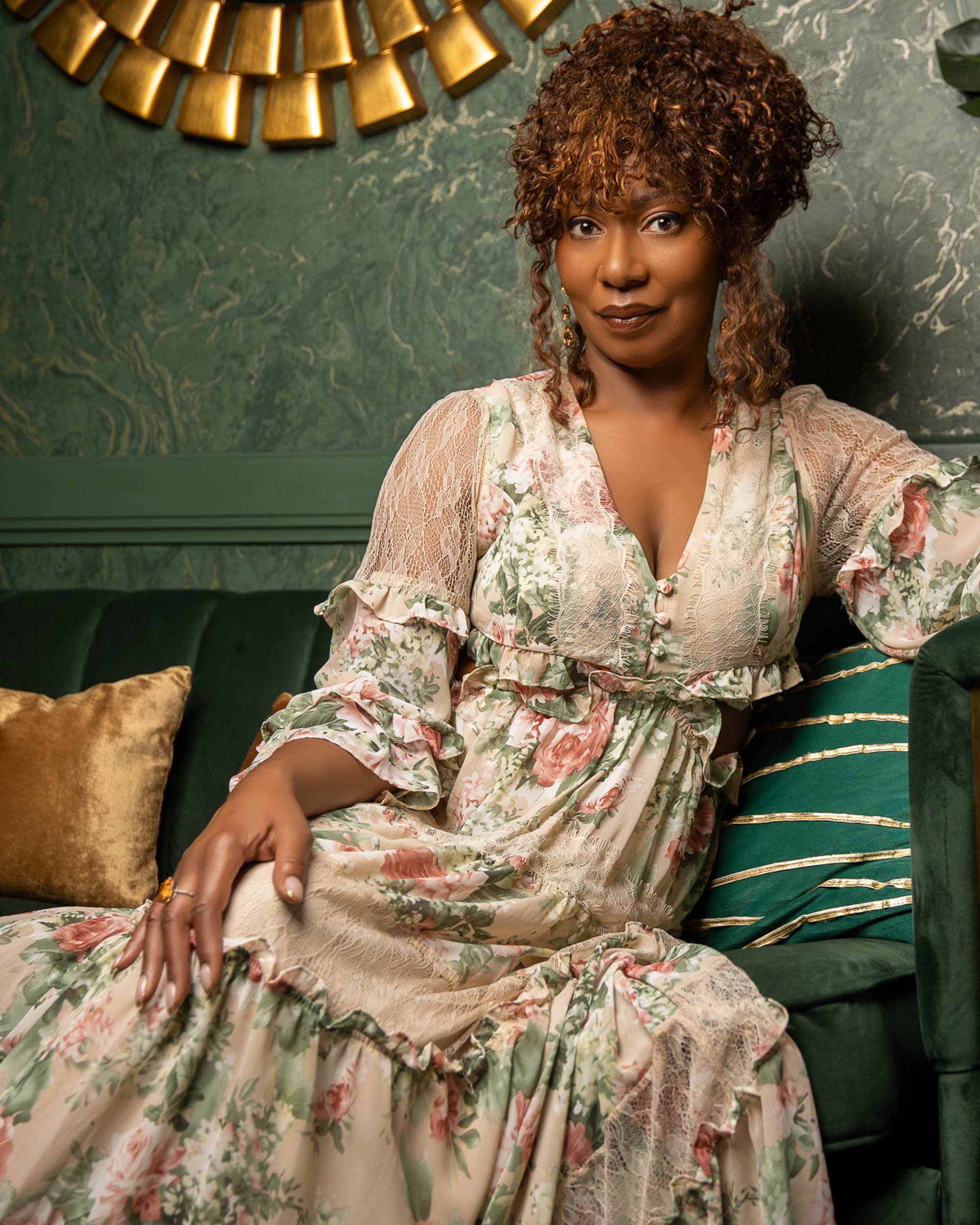 Personal branding portrait of a woman in a floral dress seated in an emerald interior