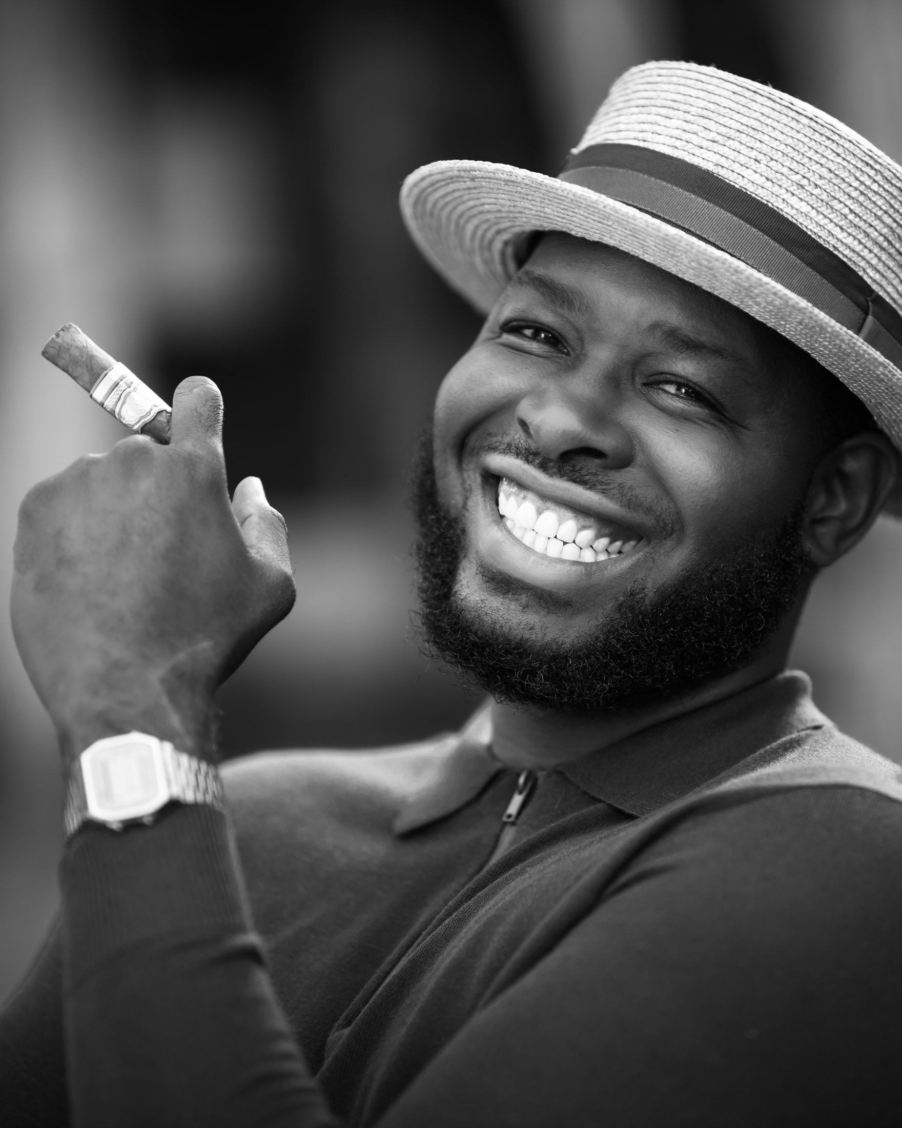 Black-and-white personal branding portrait of a smiling man wearing a hat and holding a cigar