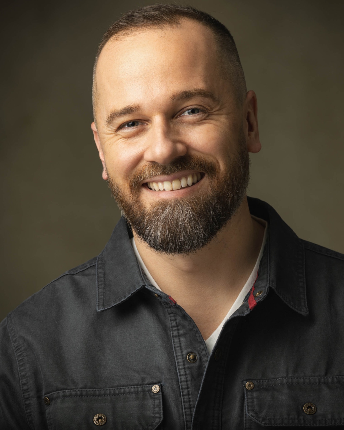 Relaxed corporate headshot of a smiling bearded man
