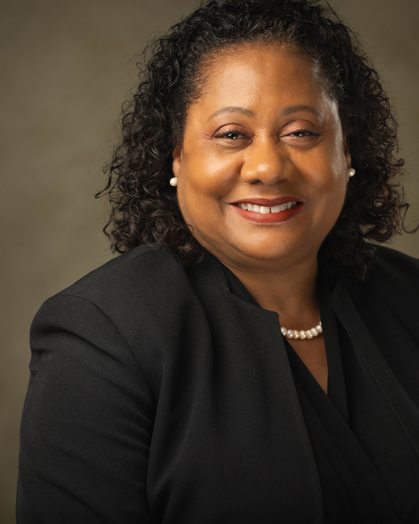 Corporate portrait of a smiling woman in a black blazer and pearl earrings