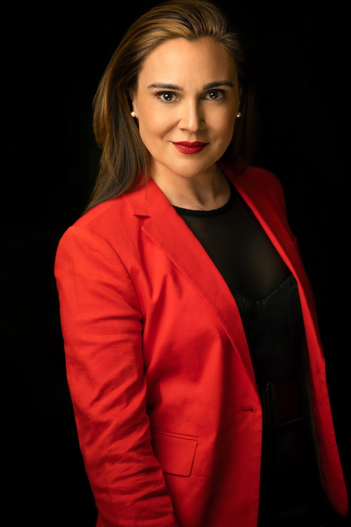 Studio corporate portrait of a woman in a vivid red blazer against a black background