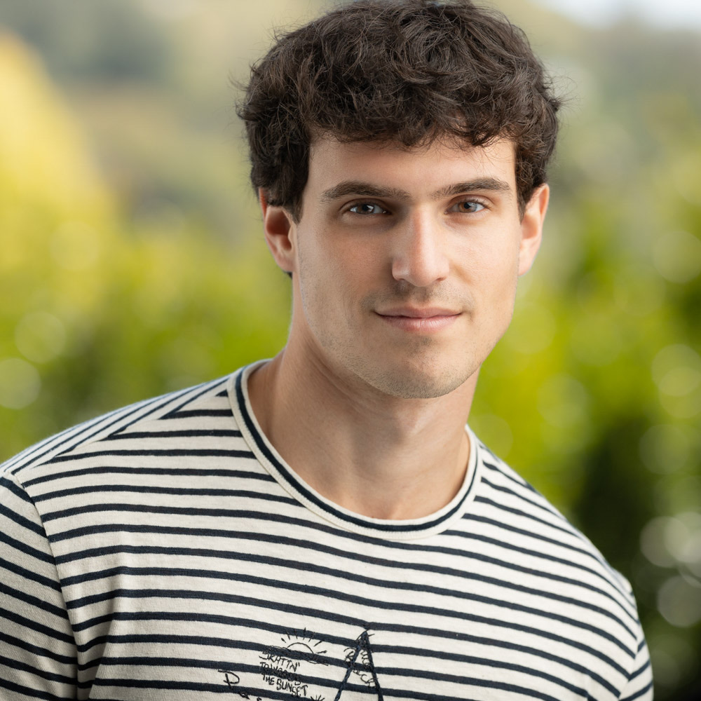 Casual outdoor portrait of a young man in a striped shirt against soft greenery