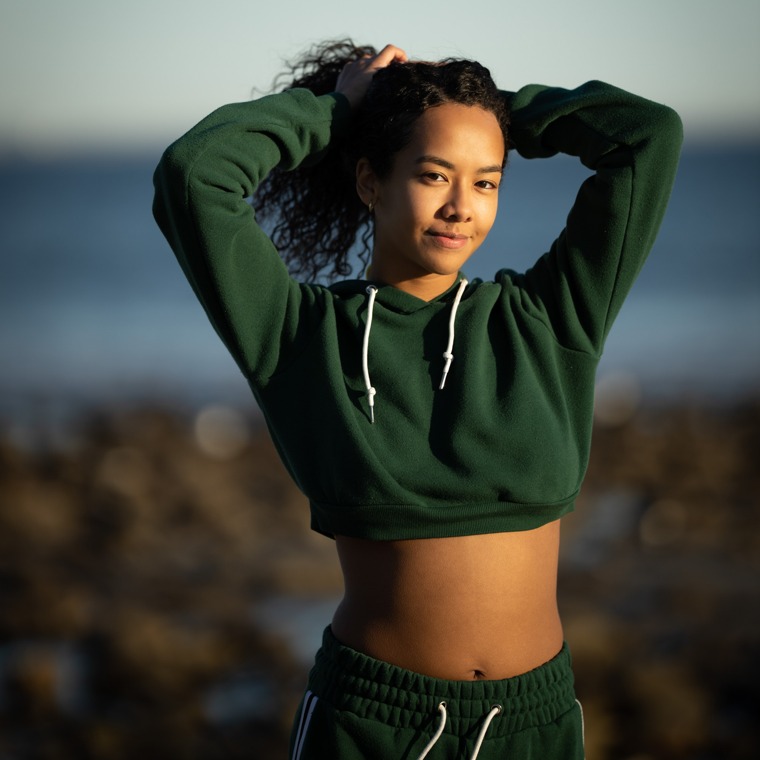 Woman in a deep green sweatshirt posing outdoors in warm coastal light
