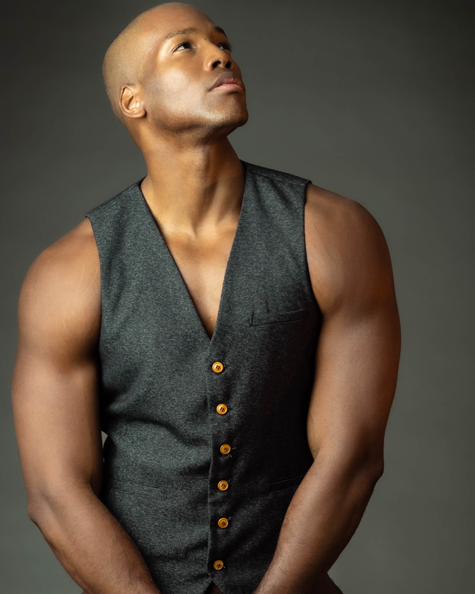 Man in a tailored sleeveless gray vest looking upward in a studio portrait