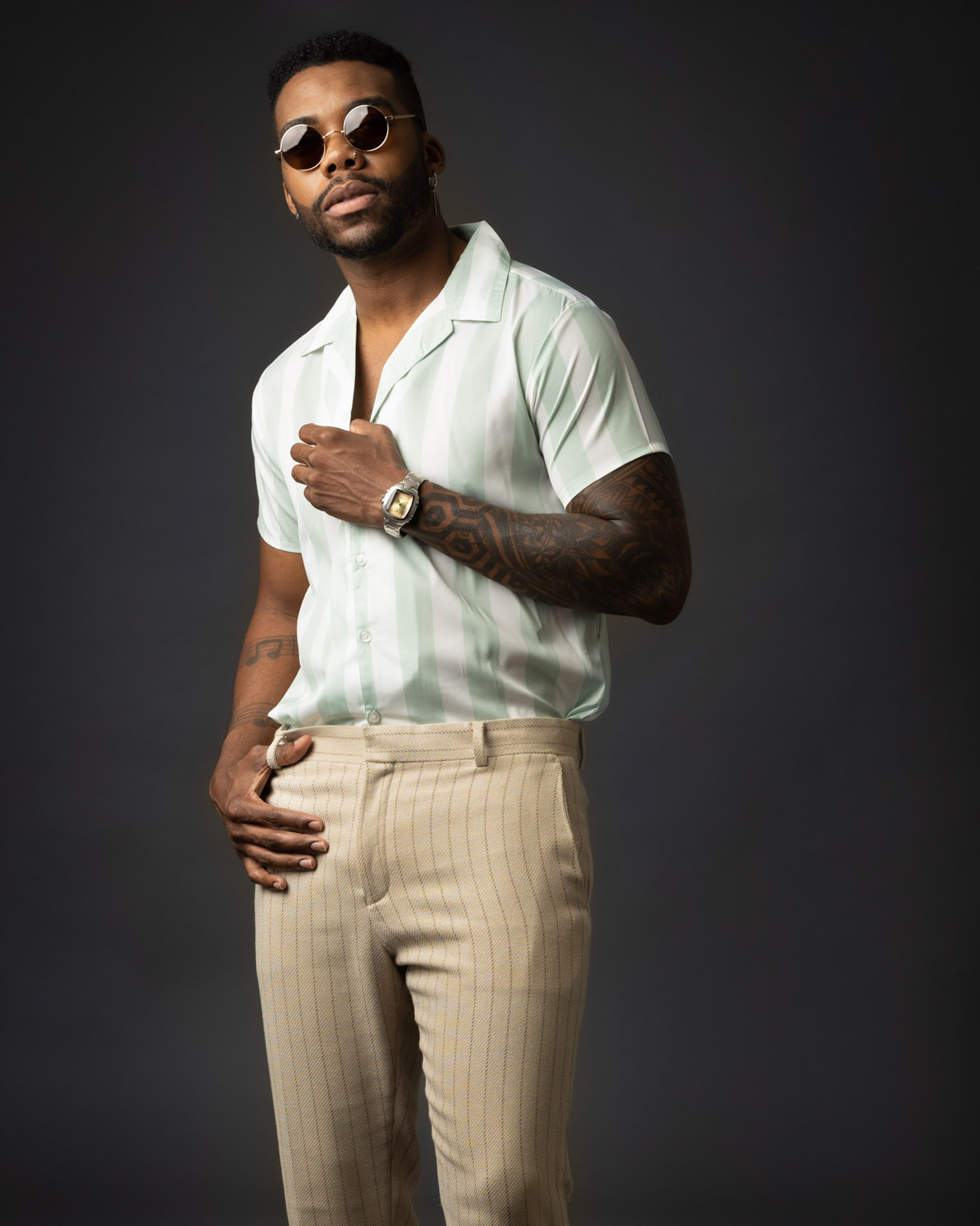 Man in sunglasses and a striped shirt posing against a dark studio background