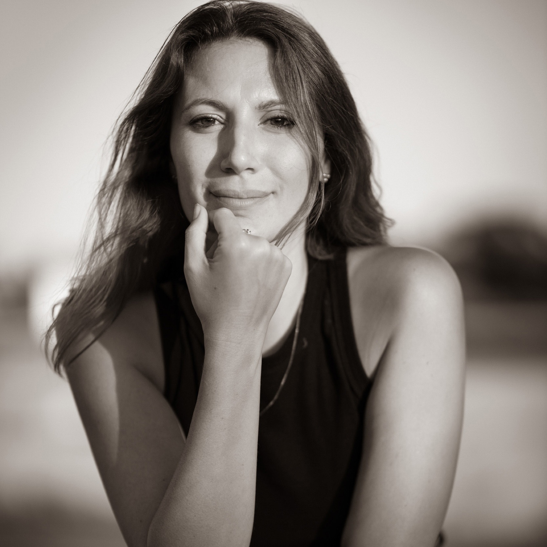 Black and white portrait of a woman resting her chin on her hand, photographed outdoors in soft light